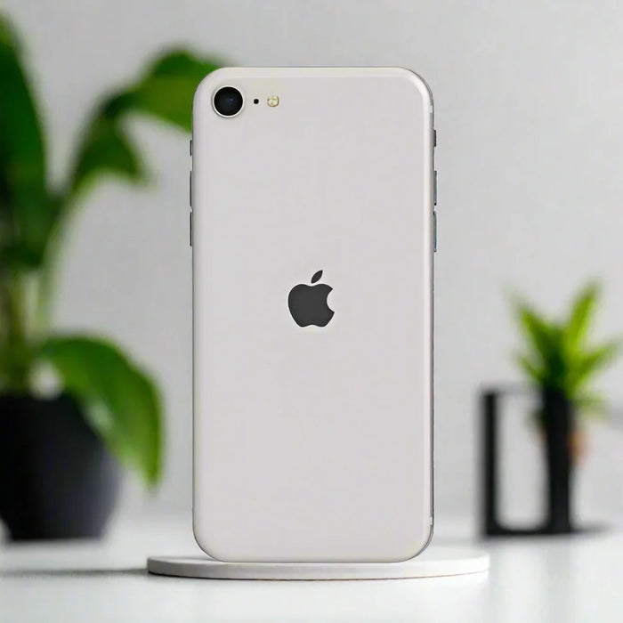 The Apple iPhone SE 2022 3rd Gen 64GB Starlight Unlocked AU STOCK Smartphone stands upright on a circular platform, with blurred green plants and a white wall in the background for a clean, minimal look.