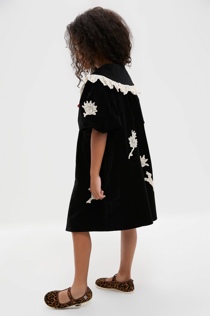 A young girl stands sideways in a Sea New York velveteen lace applique dress with white embroidered details, paired with leopard print flat shoes.
