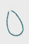 The Alexa Leigh Turquoise Opal Necklace features round teal beads, a gold clasp, and an adjustable length chain, all arranged in a loop.