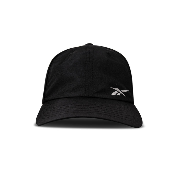 The Reebok Flow Piped Cap in black features a curved brim, a small white logo on the front left, and is made from recycled polyester with a moisture-wicking sweatband. Shown against a plain white background.