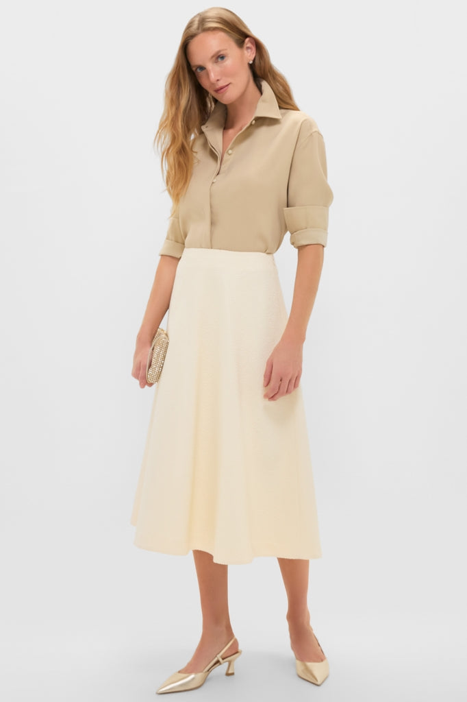 Model wearing the Gold Noelle Button Down tucked into a high-waisted skirt, paired with metallic heels and a clutch for a classic, effortless, high-end look.