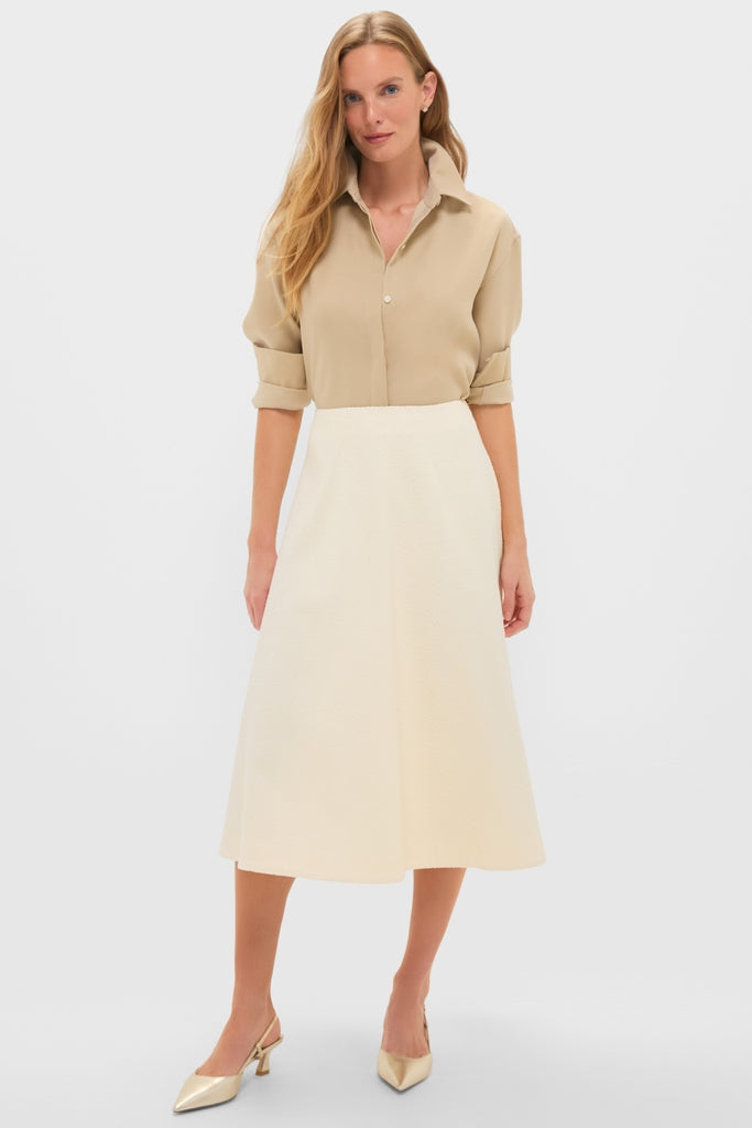 Model wearing the Gold Noelle Button Down with gold shine, paired with a high-waisted midi skirt and metallic slingback heels, embodying classic and effortless high-end style.