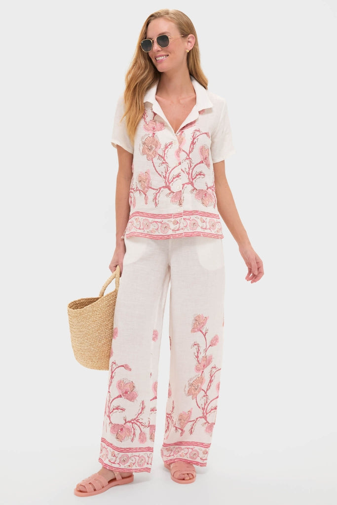 Model wearing Hibiscus Bloom Pink Florentine Pants with a relaxed, floral print. Styled with matching shirt, sunglasses, and a tote, for an effortless, high-end, and fun summer look.