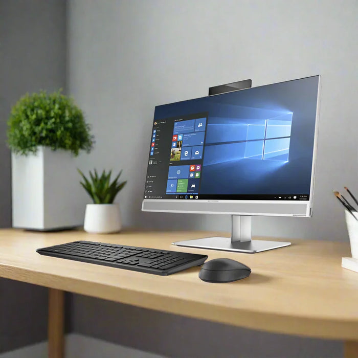 An HP EliteOne 800 G3 AIO with i7, 16GB RAM, 256GB SSD, and 23.8 display sits on a wooden desk with keyboard and mouse. Windows 10 Pro is on the screen. Two potted plants decorate the gray-walled background.
