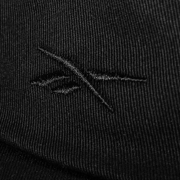 Close-up of black cotton twill fabric on the Reebok Logo S-Vector Cap, featuring a stitched abstract crossed-lines logo and textured pattern on an adjustable snapback.