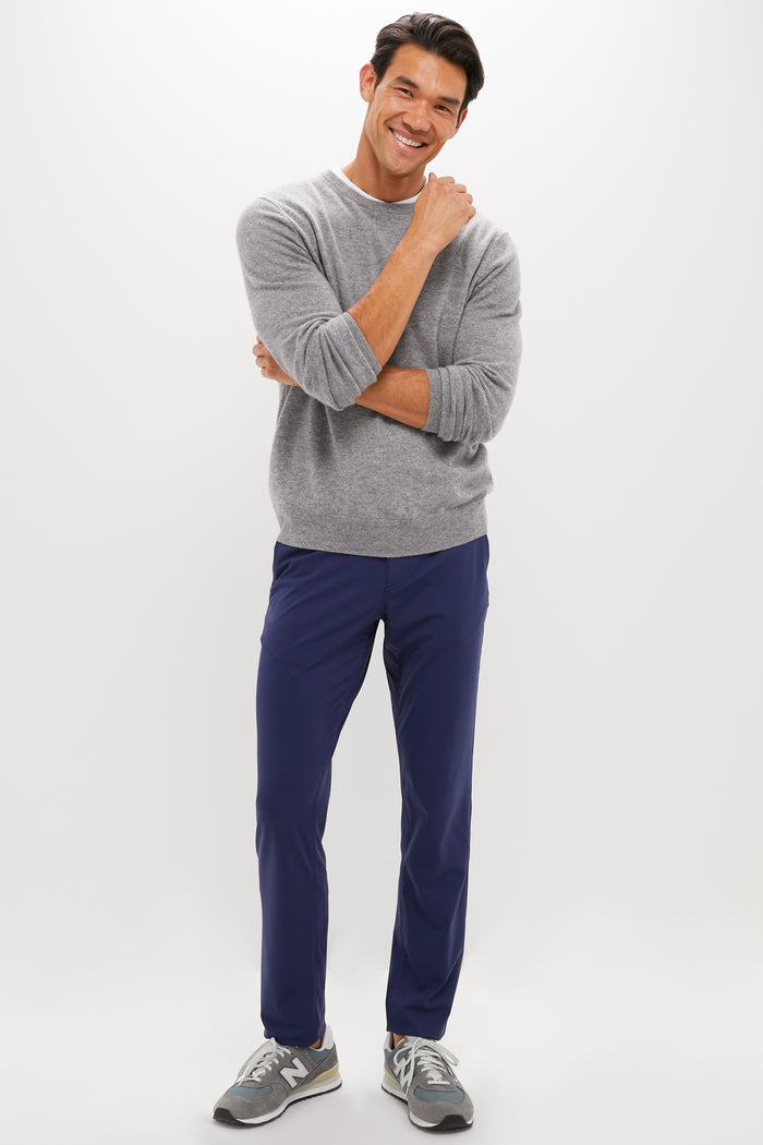 A man smiles with one hand on his chin, wearing a gray sweater, blue REDVANLY CLIMATEcomfort pull-on golf trousers, and gray New Balance sneakers against a plain white background.