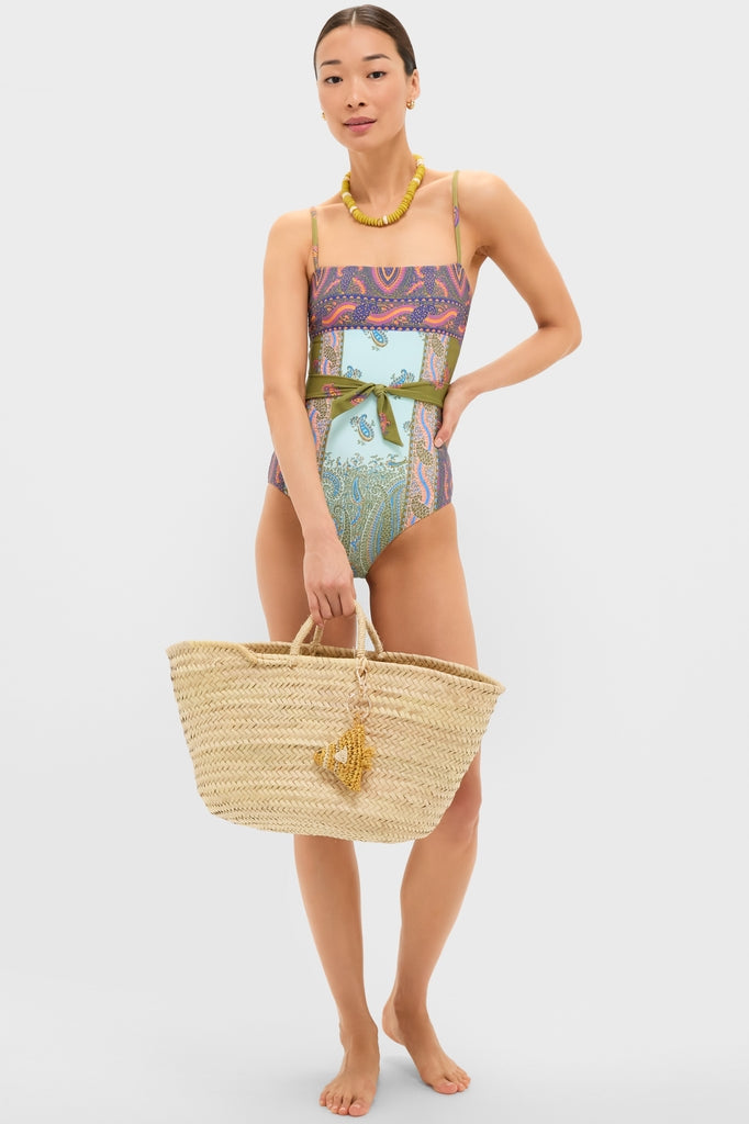Pastel Patchwork Lucent One Piece on model with paisley prints, classic straw tote, and chunky necklace. Features full coverage, adjustable straps, embodying effortless, fun, high-end style.
