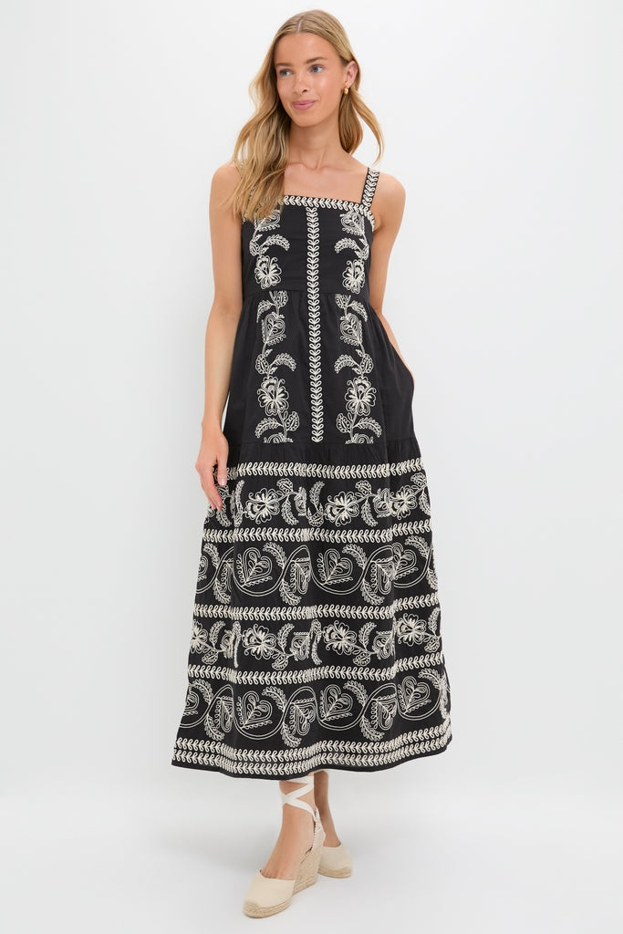 Young woman models the Sweetheart Rio Dress, a classic, high-end black maxi with white folk-inspired embroidery, an empire waist, tiered skirt, and effortless side pockets.