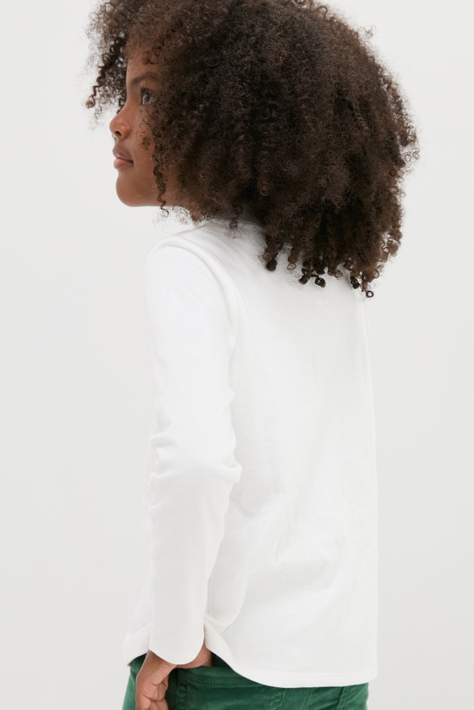 Young child in profile wearing Oso & Me's classic White Frank T-Neck, showcasing an effortless, high-end turtleneck style, ideal for layering and everyday fun.